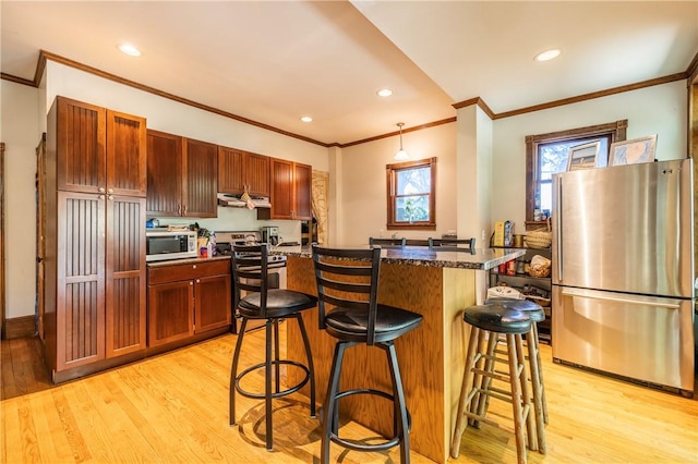 kitchen with a breakfast bar, ventilation hood, light wood-style floors, and appliances with stainless steel finishes