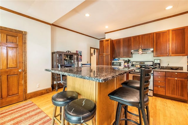 kitchen featuring under cabinet range hood, a breakfast bar area, light wood-type flooring, ornamental molding, and stainless steel gas range