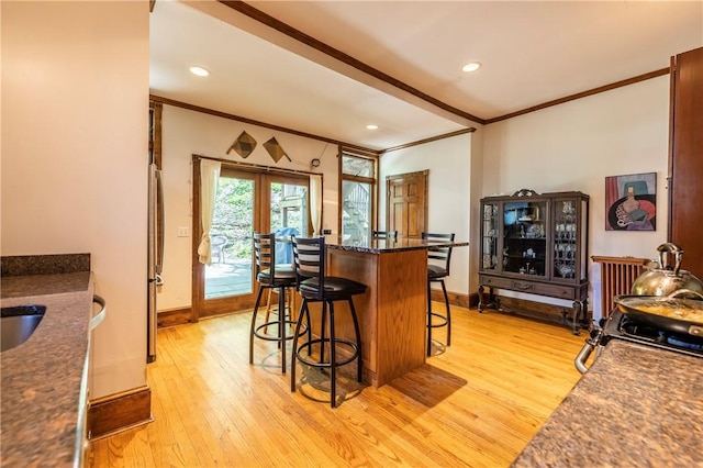 kitchen featuring freestanding refrigerator, light wood-style flooring, a breakfast bar, and crown molding