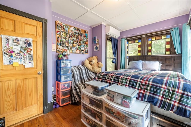 bedroom with a drop ceiling, multiple windows, a wall unit AC, and wood finished floors