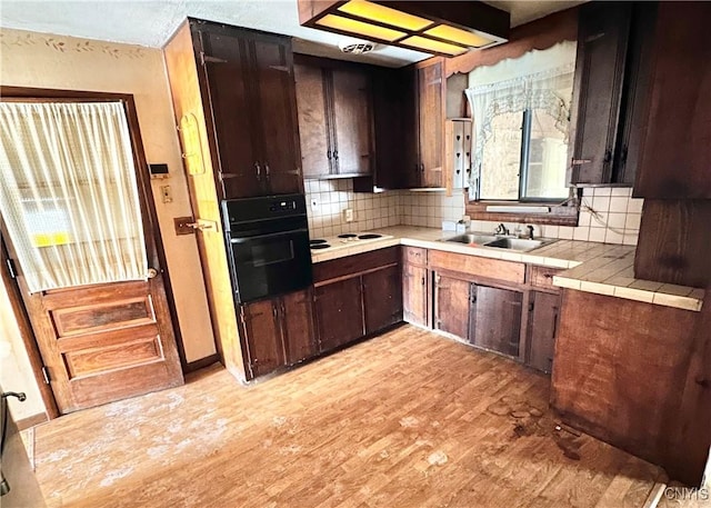 kitchen featuring tile counters, light wood-style flooring, oven, dark brown cabinets, and a sink