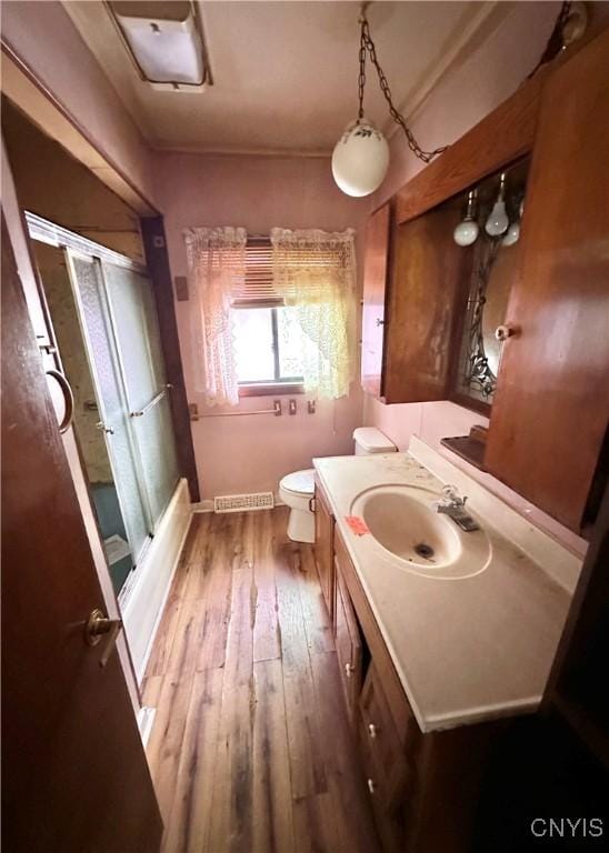 bathroom featuring bath / shower combo with glass door, visible vents, toilet, vanity, and wood finished floors