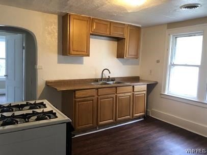 kitchen featuring arched walkways, brown cabinets, a sink, and white gas range oven