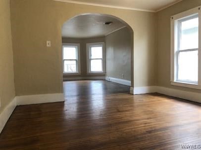 spare room with arched walkways, dark wood-type flooring, crown molding, and a healthy amount of sunlight