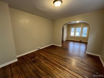 empty room featuring arched walkways, dark wood finished floors, and baseboards