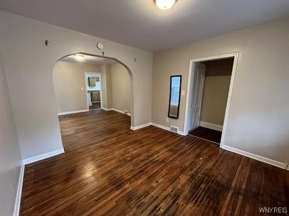 empty room featuring baseboards, arched walkways, and dark wood finished floors