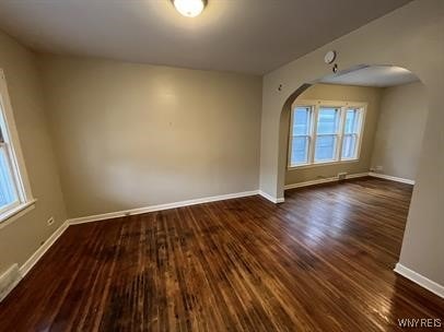 unfurnished room featuring arched walkways, dark wood finished floors, and baseboards