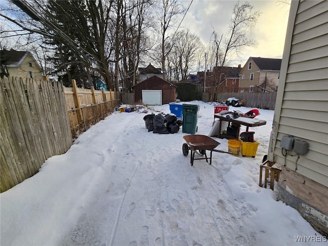 snowy yard with a garage, a fenced backyard, and an outbuilding