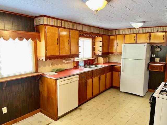 kitchen featuring white appliances, light countertops, wood walls, light floors, and a sink