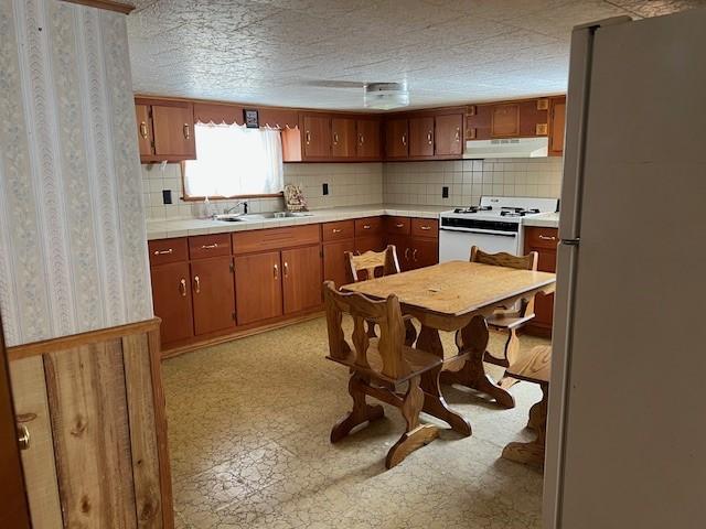 kitchen with white appliances, under cabinet range hood, light countertops, and brown cabinetry