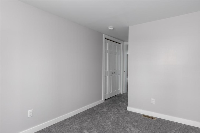 spare room with visible vents, dark carpet, and baseboards