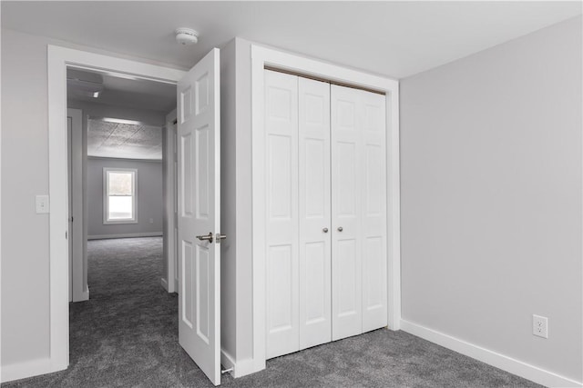 unfurnished bedroom with baseboards, dark colored carpet, and a closet