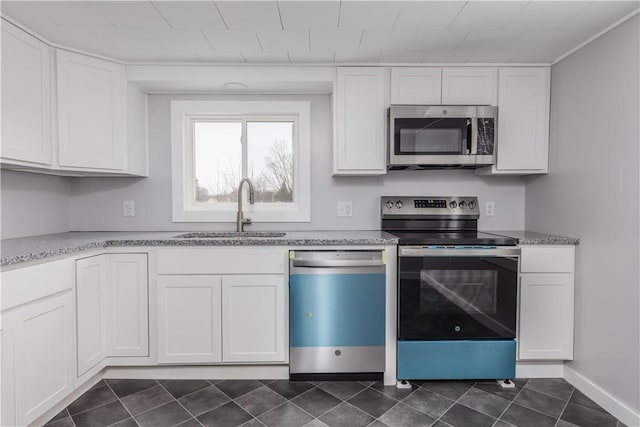 kitchen featuring light stone counters, appliances with stainless steel finishes, white cabinetry, a sink, and dark tile patterned floors