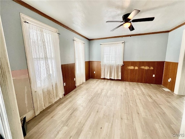 empty room with a wainscoted wall, crown molding, light wood-style flooring, and ceiling fan