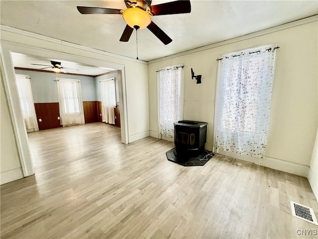 unfurnished room featuring visible vents, wainscoting, light wood finished floors, a wood stove, and crown molding