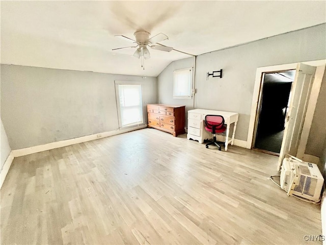 unfurnished bedroom with light wood-style floors, lofted ceiling, an AC wall unit, and baseboards