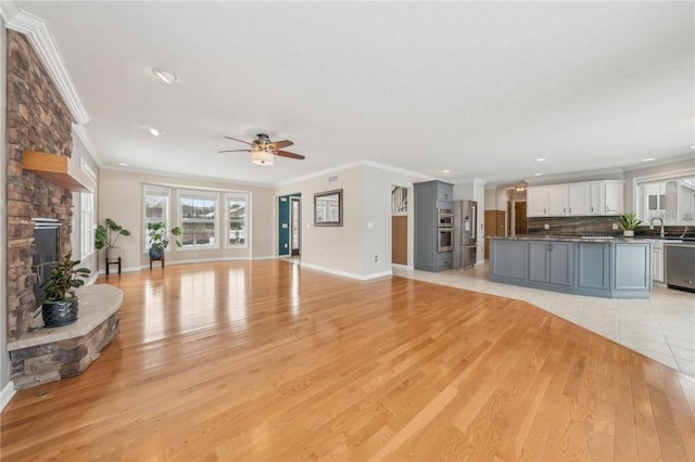 unfurnished living room with light wood finished floors, baseboards, ornamental molding, and a stone fireplace