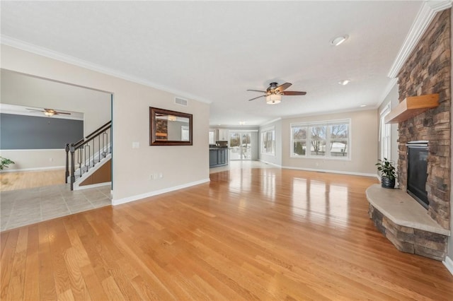 unfurnished living room featuring crown molding, a fireplace, visible vents, stairway, and light wood-type flooring