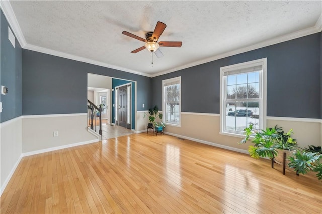 exercise room featuring ornamental molding, light wood-type flooring, a textured ceiling, and baseboards