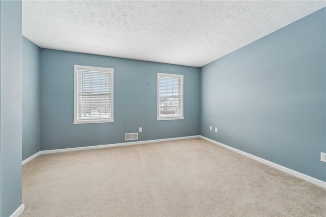 empty room featuring light carpet, a textured ceiling, visible vents, and baseboards