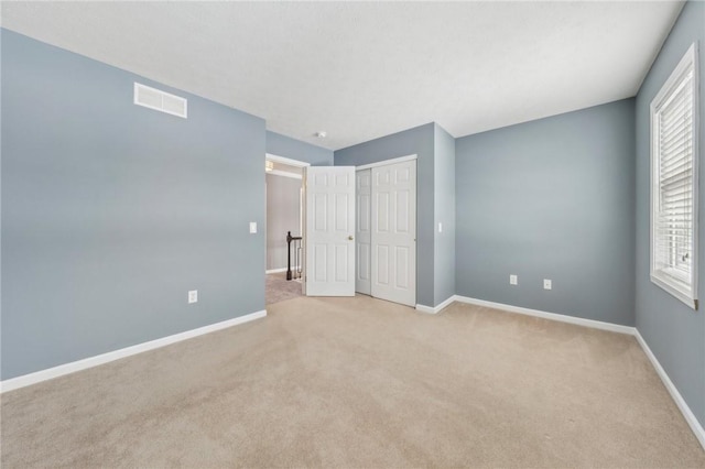 unfurnished bedroom with a closet, light colored carpet, visible vents, and baseboards