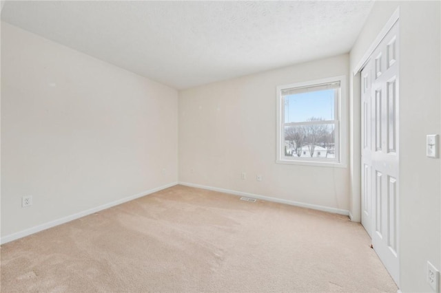 spare room featuring visible vents, baseboards, a textured ceiling, and light colored carpet