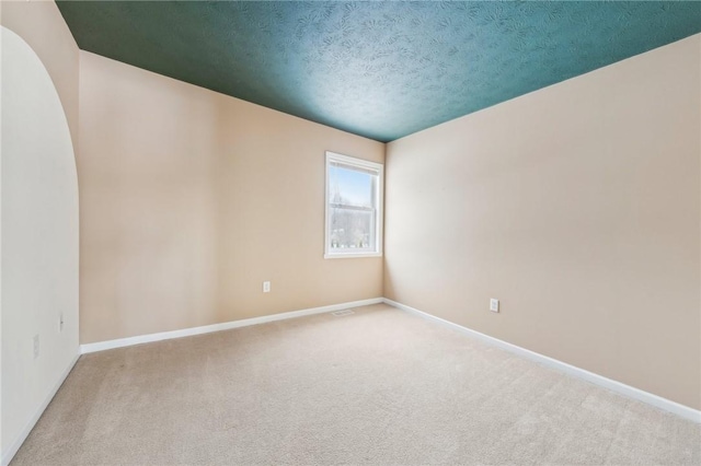 spare room with light colored carpet, a textured ceiling, and baseboards