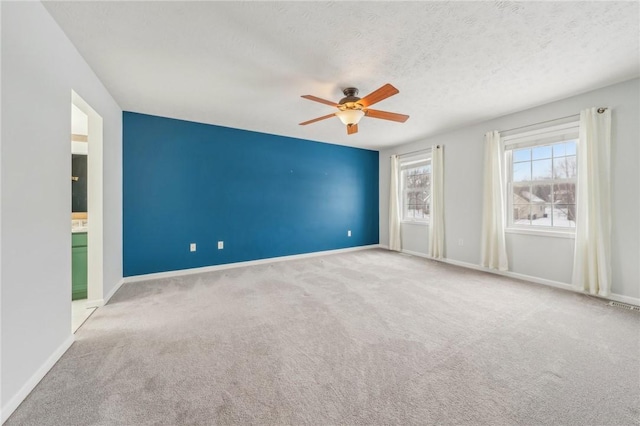 carpeted spare room with a ceiling fan, baseboards, and a textured ceiling