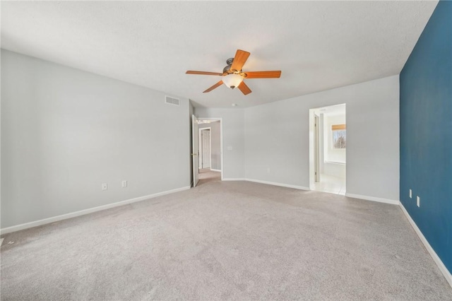 carpeted spare room with baseboards, visible vents, and a ceiling fan