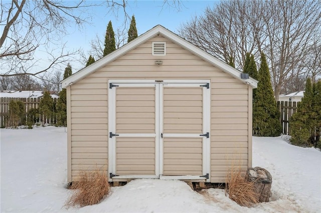 snow covered structure with fence, an outdoor structure, and a shed