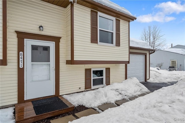 snow covered property entrance featuring an attached garage