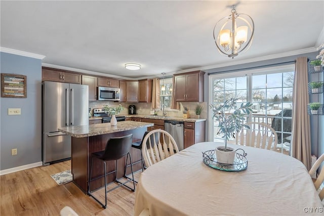 kitchen featuring light wood finished floors, a center island, decorative light fixtures, stainless steel appliances, and crown molding