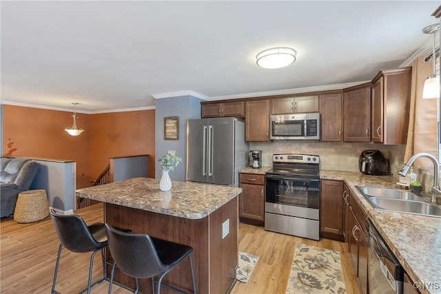 kitchen featuring a sink, appliances with stainless steel finishes, light wood-type flooring, a center island, and decorative light fixtures