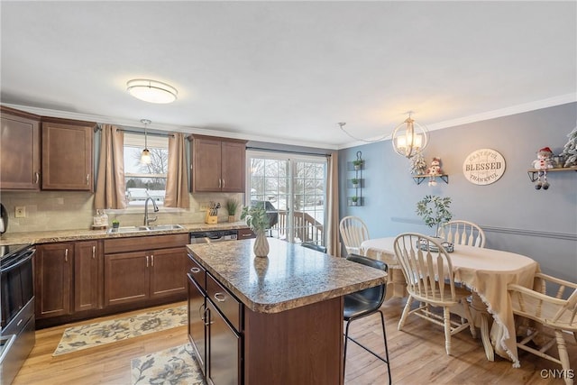 kitchen with a sink, a kitchen island, hanging light fixtures, ornamental molding, and light wood finished floors