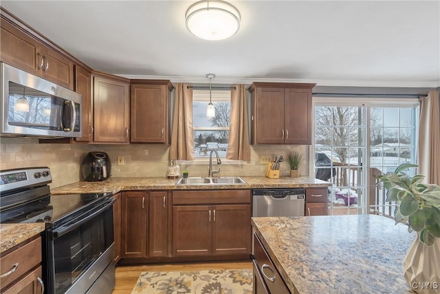 kitchen with light stone counters, stainless steel appliances, a sink, and pendant lighting