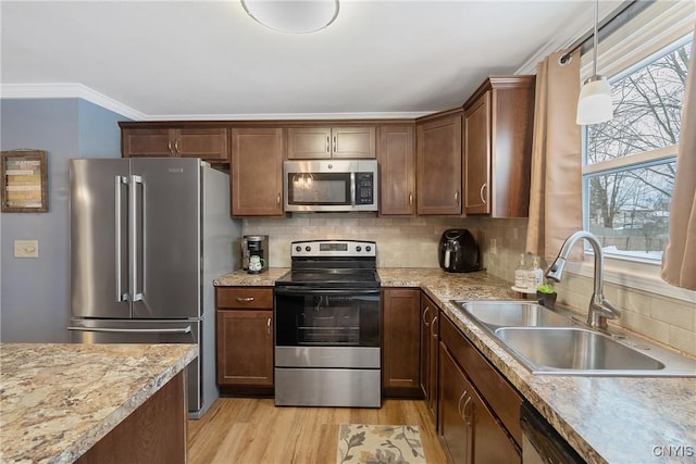 kitchen with light wood-style flooring, stainless steel appliances, a sink, backsplash, and pendant lighting