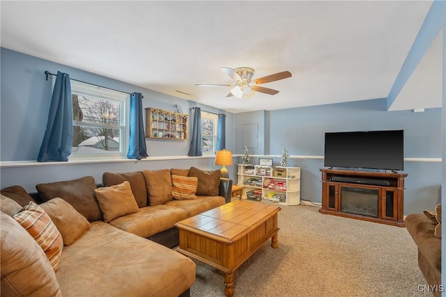 living area featuring carpet, a glass covered fireplace, and a ceiling fan