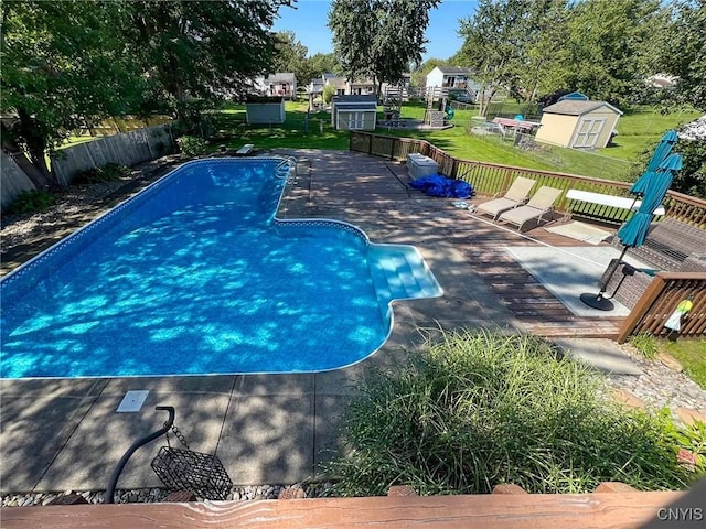 view of swimming pool featuring a patio, fence, a wooden deck, a fenced in pool, and a storage unit