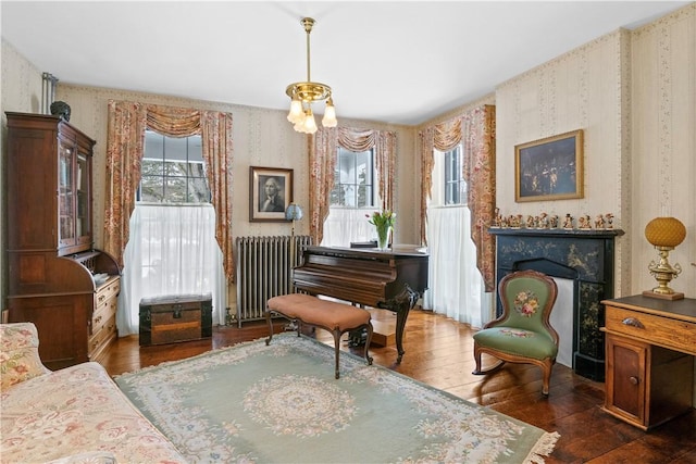 living area with a fireplace, dark wood finished floors, radiator heating unit, an inviting chandelier, and wallpapered walls