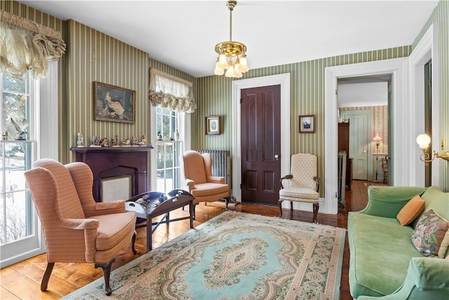 living area featuring wood finished floors, a fireplace, a notable chandelier, and wallpapered walls