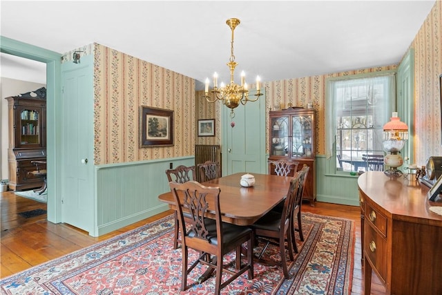 dining area featuring wood-type flooring, a wainscoted wall, a notable chandelier, and wallpapered walls