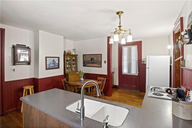 kitchen with dark wood-style floors, hanging light fixtures, wainscoting, a sink, and white appliances