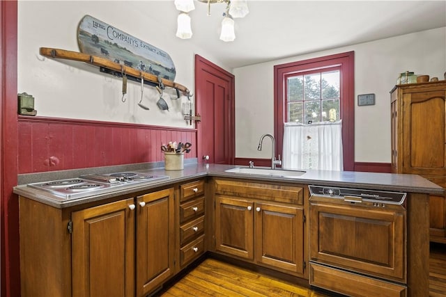 kitchen featuring a peninsula, dark countertops, a sink, and wainscoting