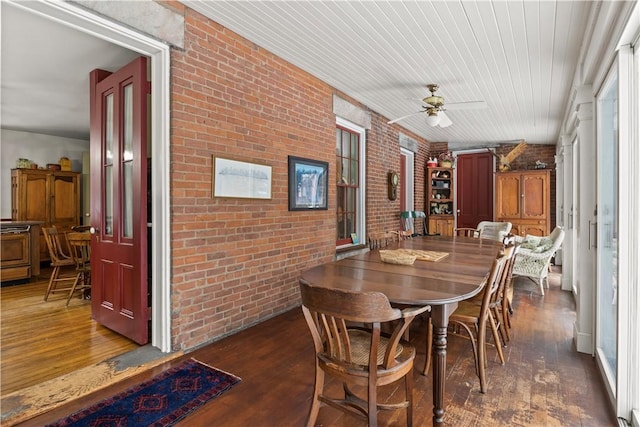 dining room featuring dark wood-type flooring, ceiling fan, and brick wall