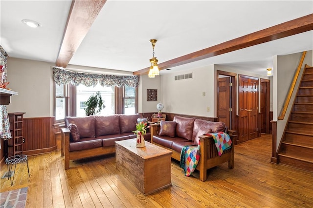 living area featuring visible vents, stairs, wainscoting, light wood finished floors, and beamed ceiling