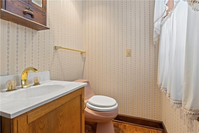 bathroom with wood finished floors, vanity, toilet, and wallpapered walls