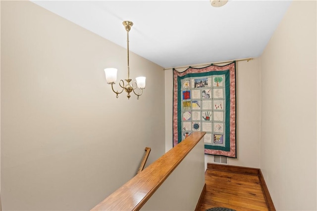 hall with visible vents, an upstairs landing, baseboards, hardwood / wood-style floors, and an inviting chandelier