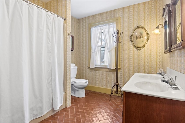 full bathroom featuring wallpapered walls, baseboards, toilet, brick floor, and a sink