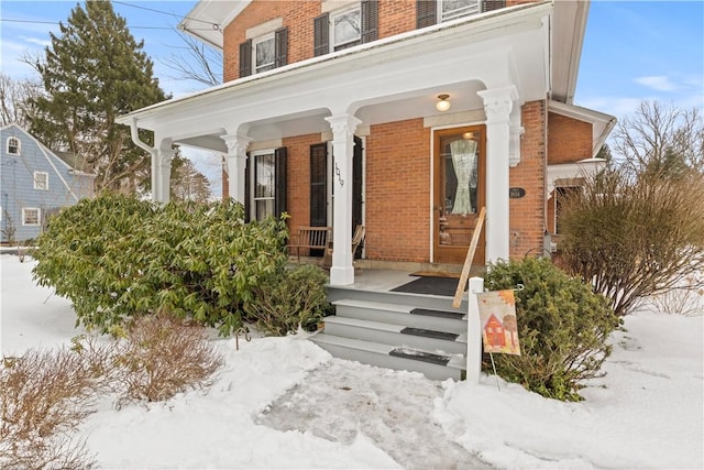 snow covered property entrance with brick siding and a porch