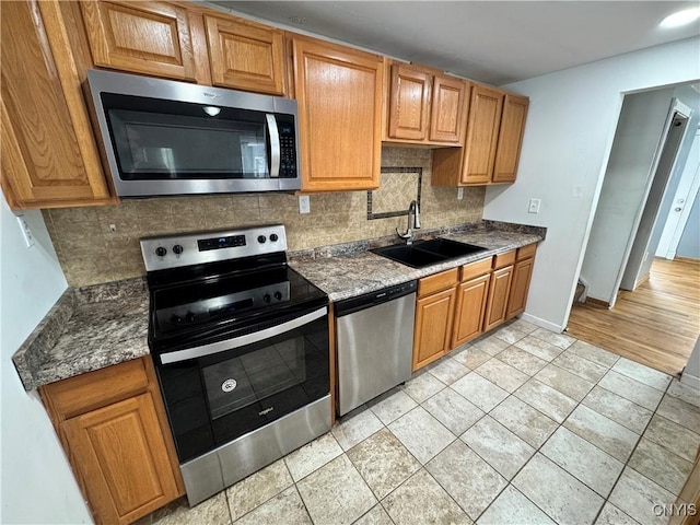 kitchen featuring appliances with stainless steel finishes, backsplash, a sink, and baseboards